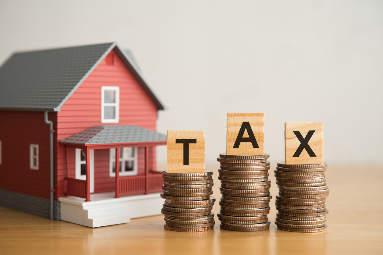 House and TAX alphabet on stack coins with white wall background. House, home, real estate property and land tax, taxation for home buying or selling, financial management concept.